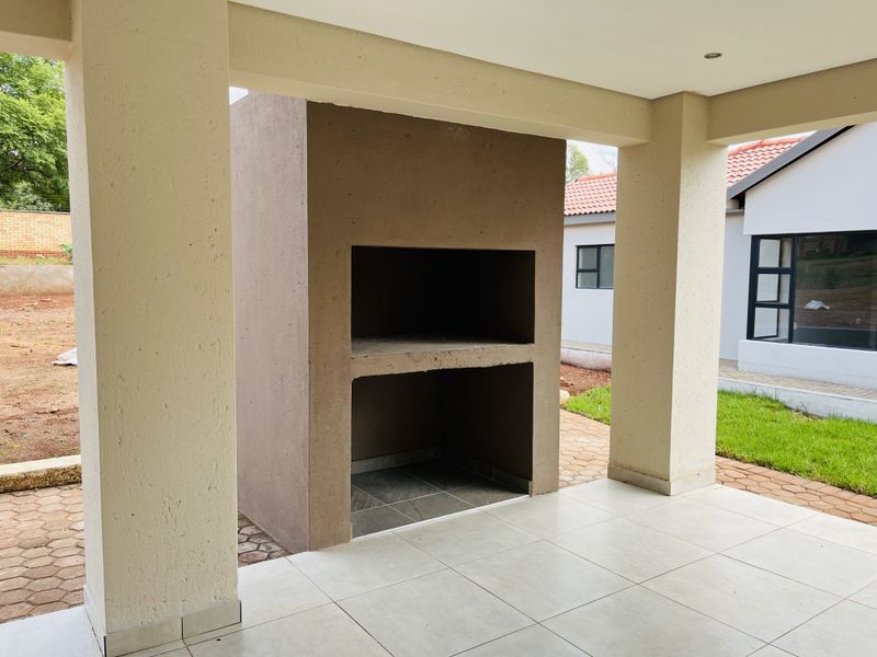 A covered patio area featuring a built-in braai, tiled flooring, and recessed lighting, offering a functional space for outdoor entertaining.