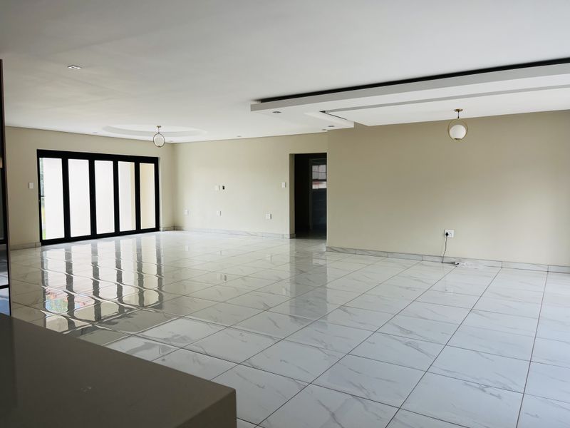 Spacious open-plan living area featuring modern white marble-look porcelain tiles, a contemporary drop ceiling with recessed lighting, and large black-framed folding doors.