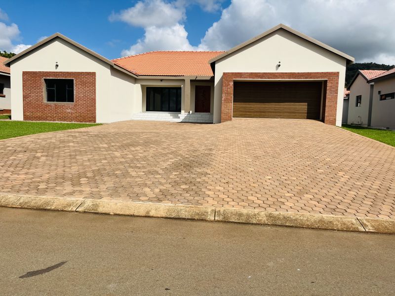 A well-maintained single-story house featuring a brick and plaster facade, a tiled roof, and a spacious paved driveway leading to a double garage.