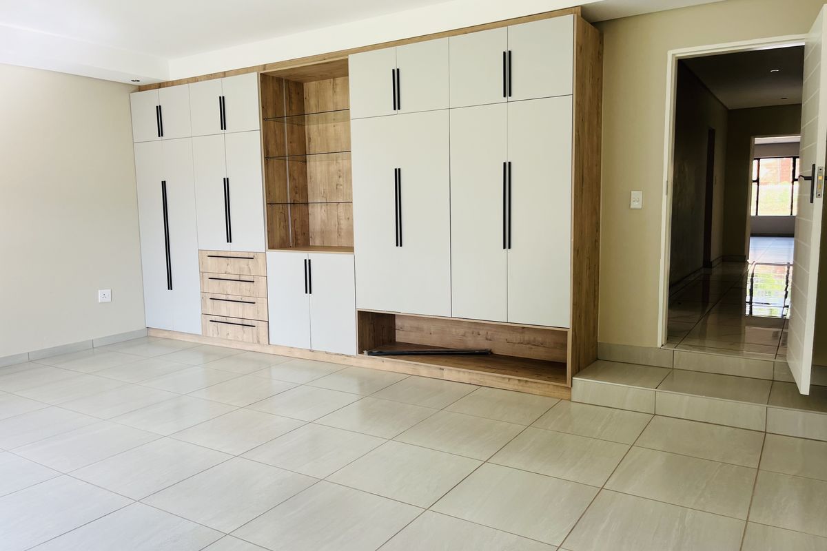 Spacious living area featuring extensive modern built-in cabinetry with a mix of wood-grain and matte finishes, complemented by neutral floor tiles.