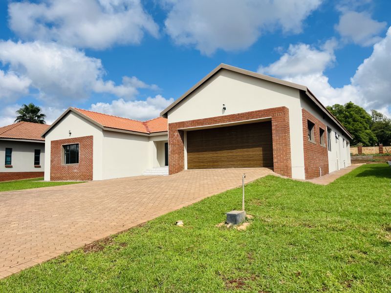 Front view of a modern single-story house featuring a brick and plaster facade, tiled roof, and a paved driveway leading to a double garage.