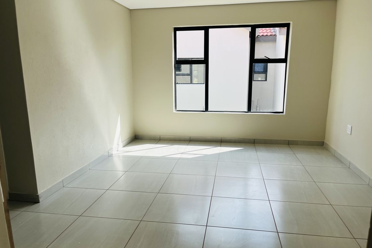 A bright, empty bedroom featuring neutral wall tones, large aluminium-framed windows, and clean tiled flooring throughout.