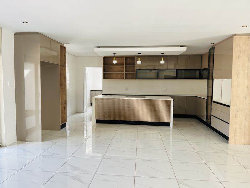 Modern, spacious kitchen featuring a central island, sleek built-in cabinetry, and high-quality tiled flooring in a bright, open-plan layout.