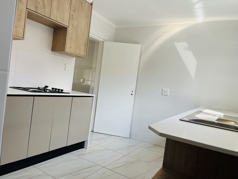 Modern kitchen featuring light-toned cabinetry, a gas hob, stainless steel sink, and clean tiled finishes throughout.