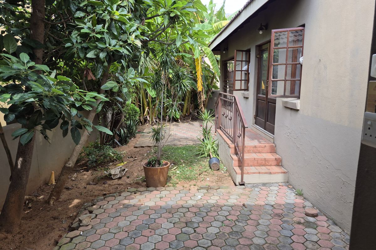A private rear garden area featuring a paved patio, brick steps leading to the dwelling, and established greenery.