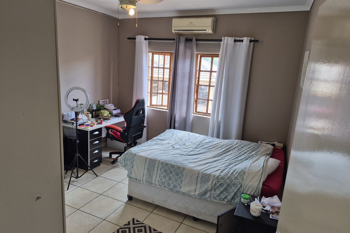 A functional bedroom featuring tiled flooring, a ceiling fan, and a wall-mounted air conditioning unit.