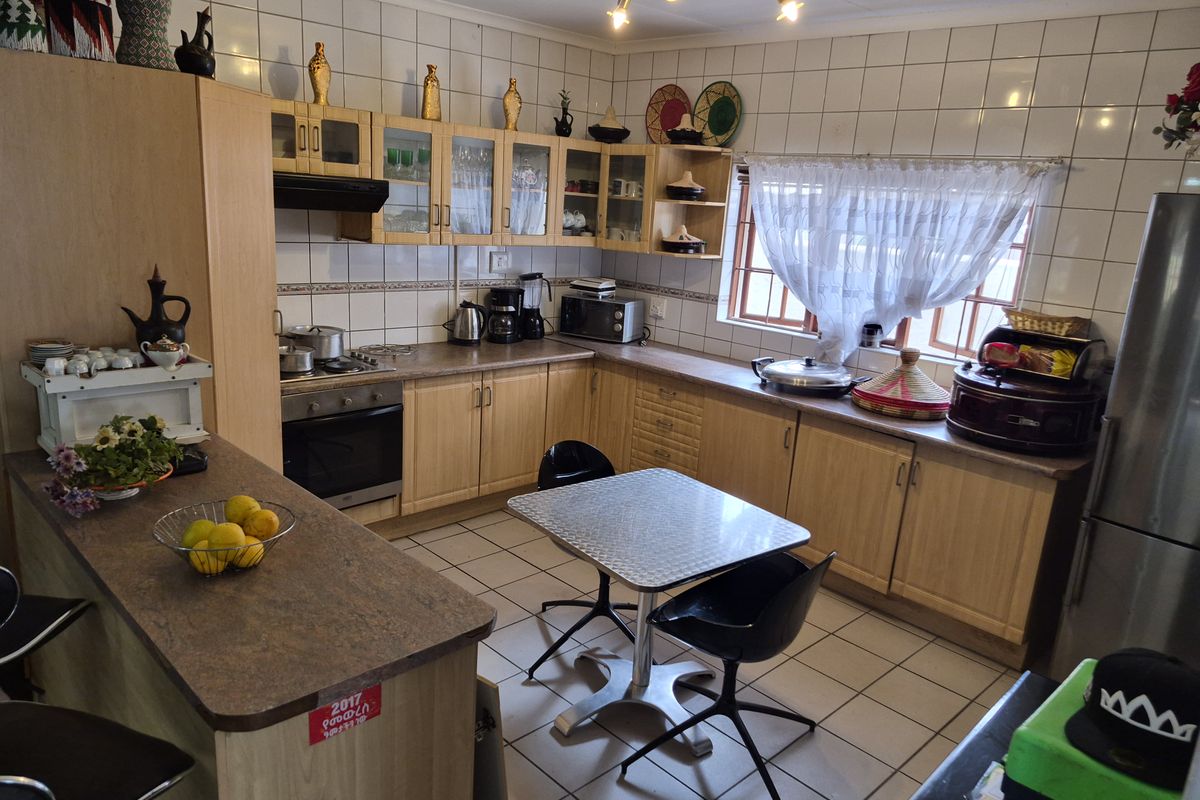 A functional kitchen featuring light wood cabinetry, tiled backsplash, built-in oven, hob, and an integrated breakfast bar area with tiled flooring.