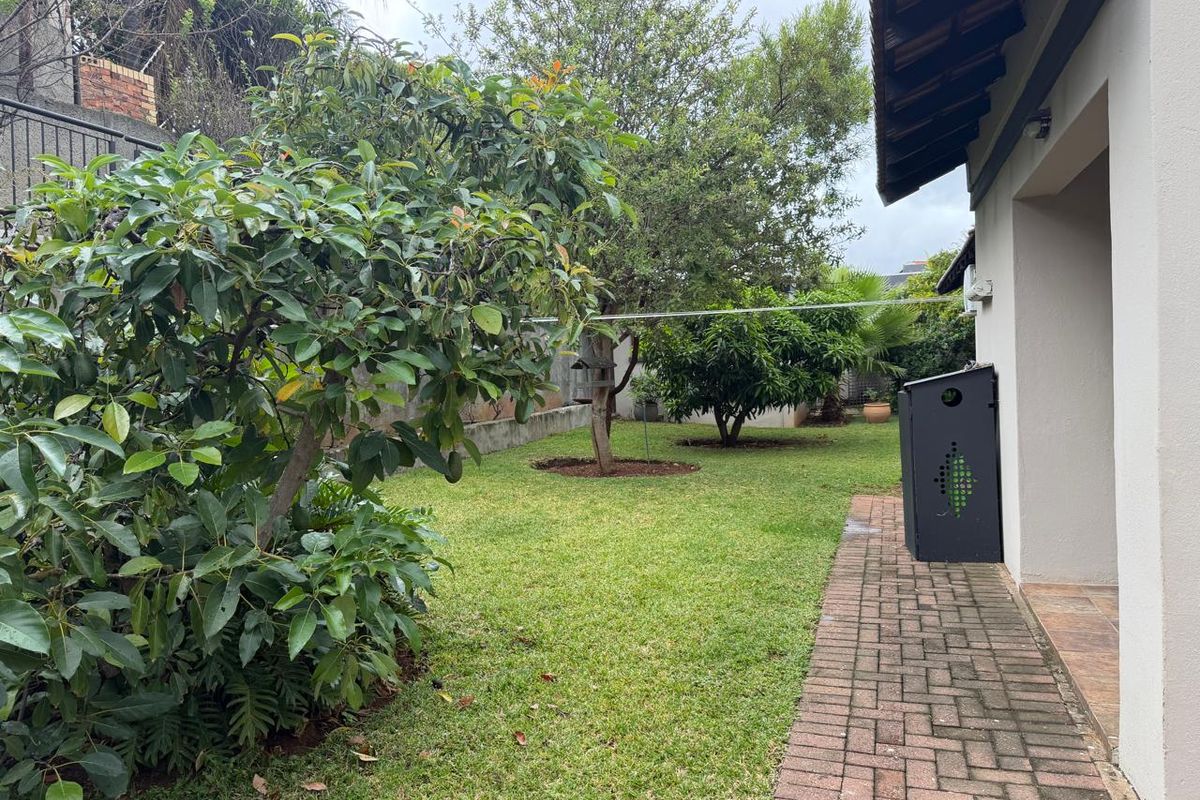 A private rear garden featuring a brick-paved walkway, established trees, and a lawn area adjacent to the house exterior.