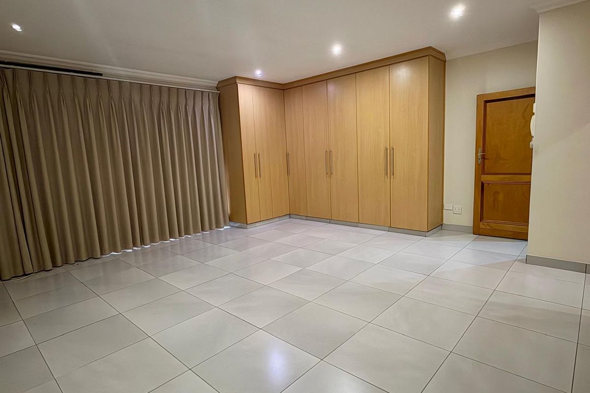 A spacious bedroom featuring light-colored floor tiles, recessed ceiling lighting, and extensive built-in wooden cabinetry for ample storage.