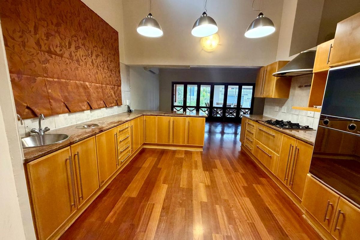 Spacious kitchen featuring warm-toned wooden cabinetry, granite countertops, built-in oven, gas hob, and stainless steel extractor fan, flowing into an open-plan living area.