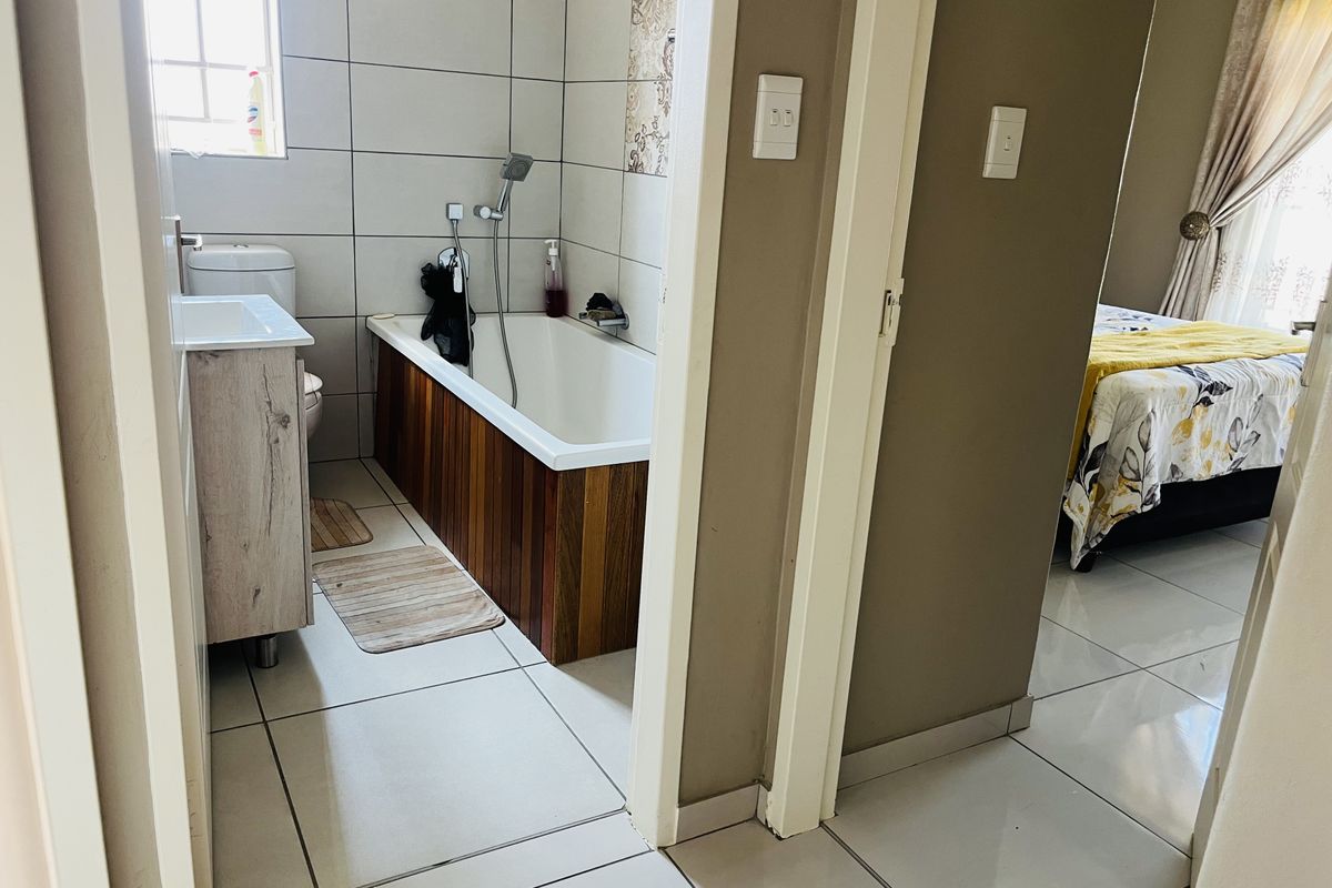 A functional bathroom featuring a bathtub with wood-look paneling, a vanity unit, and tiled flooring, adjacent to a bedroom.