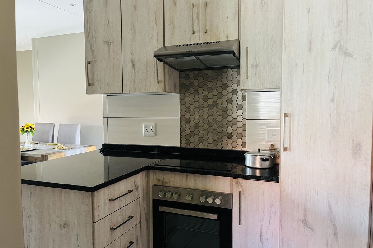 Modern kitchen featuring light wood-grain cabinetry, black granite countertops, a built-in oven with hob, and a decorative hexagonal tile backsplash.