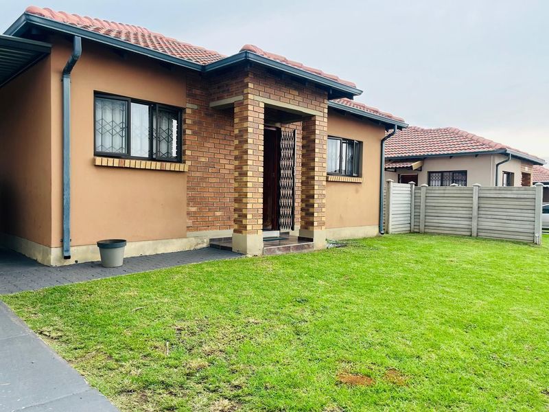 A well-maintained single-story house featuring a brick and plaster facade, tiled roof, and a neat front lawn with paved access.