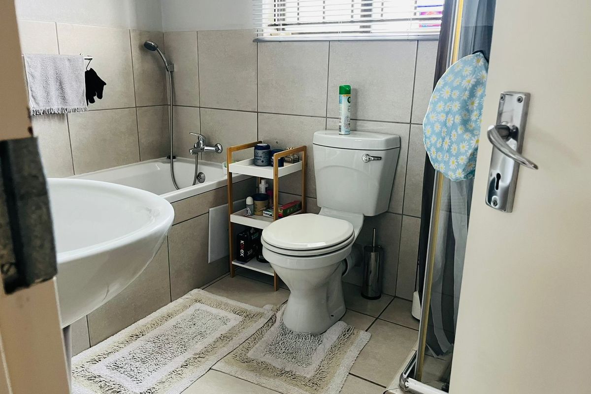 A functional bathroom featuring a bathtub, toilet, and basin with neutral wall and floor tiling.