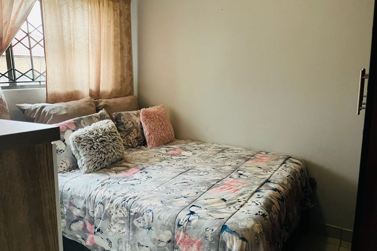 A compact bedroom featuring a built-in cupboard and security bars on the window, providing a functional and secure living space.