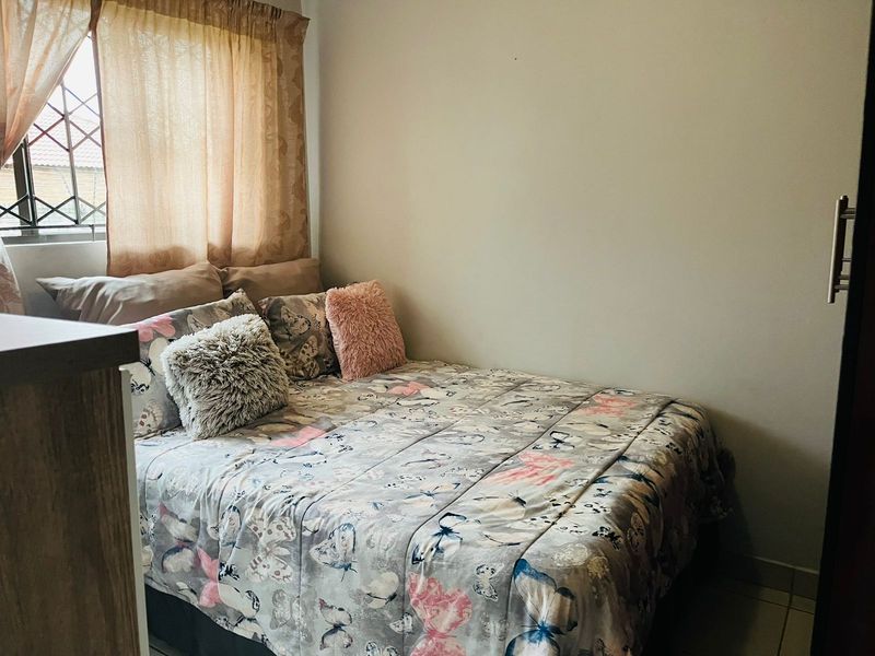 A compact bedroom featuring a built-in cupboard and security bars on the window, providing a functional and secure living space.