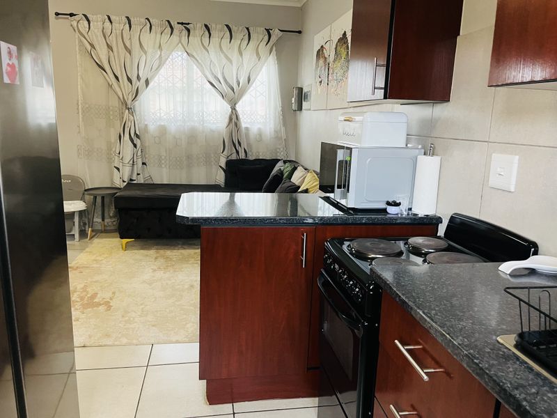 Open-plan kitchen and living area featuring dark wood cabinetry, granite countertops, electric stove, and tiled flooring throughout.