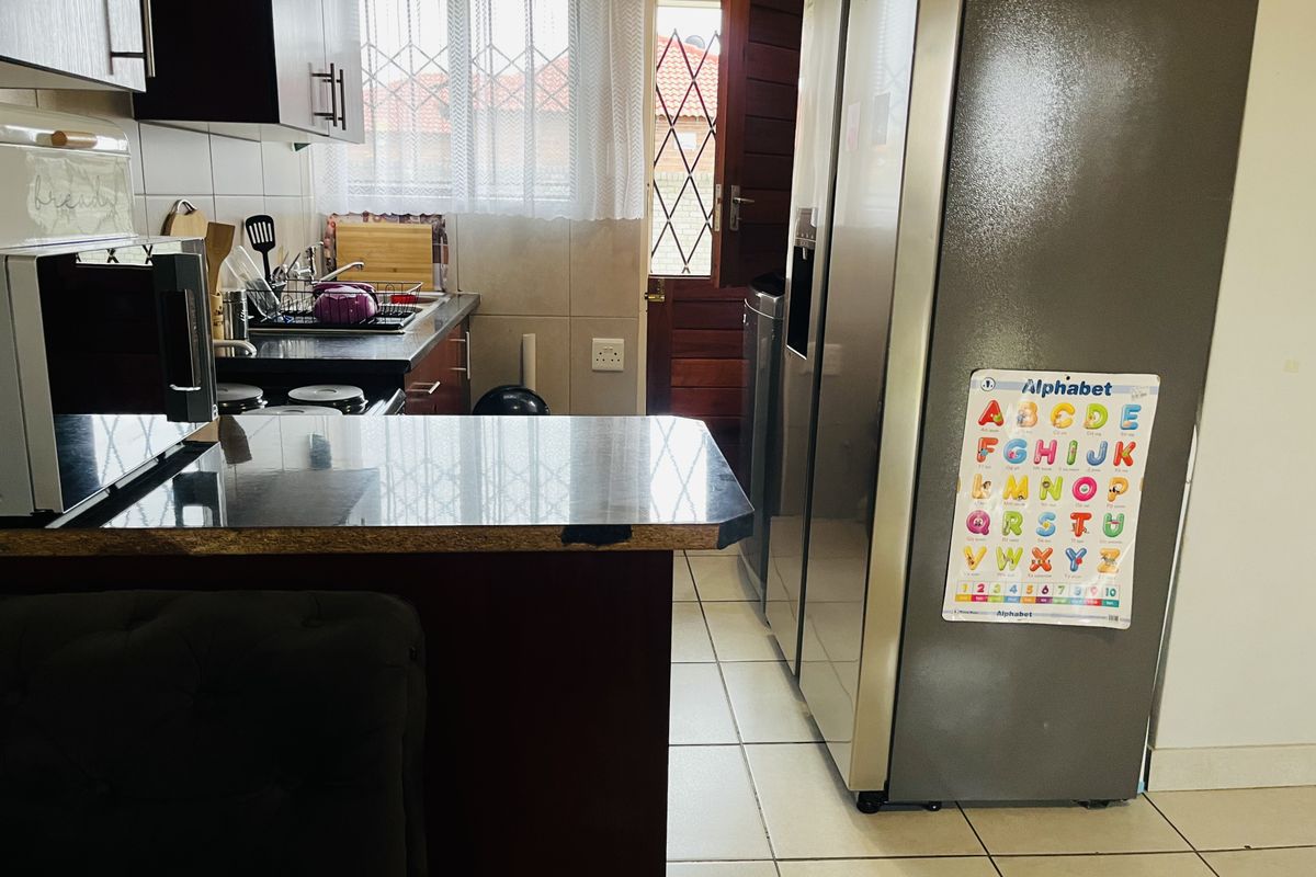 A functional kitchen featuring dark cabinetry, granite countertops, tiled flooring, and direct access to the exterior through a security-fitted door.