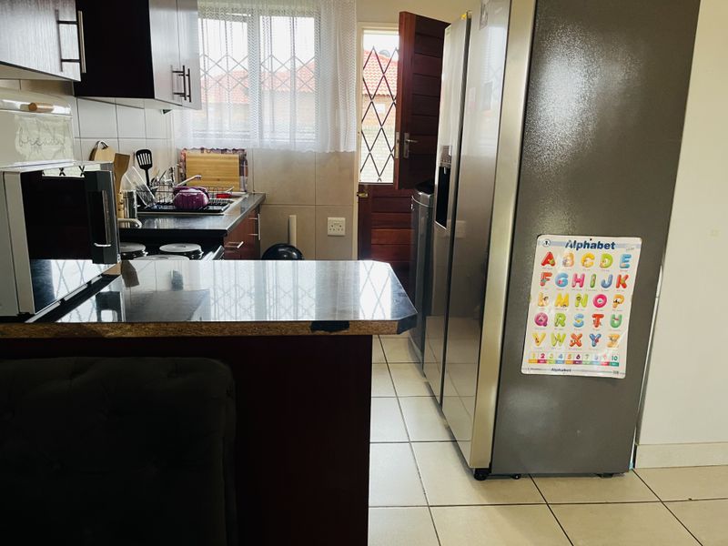 A functional kitchen featuring dark cabinetry, granite countertops, tiled flooring, and direct access to the exterior through a security-fitted door.