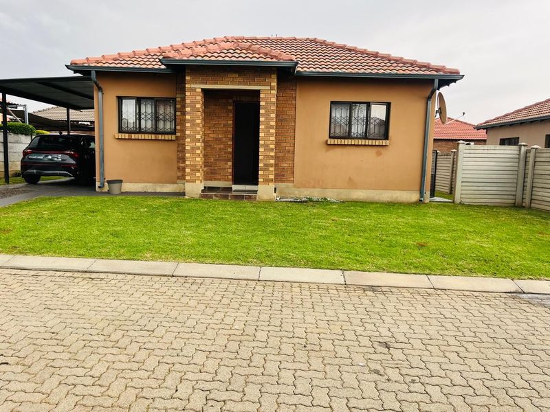 A well-maintained single-story residential home featuring a brick facade, tiled roof, security bars on windows, and an attached carport.