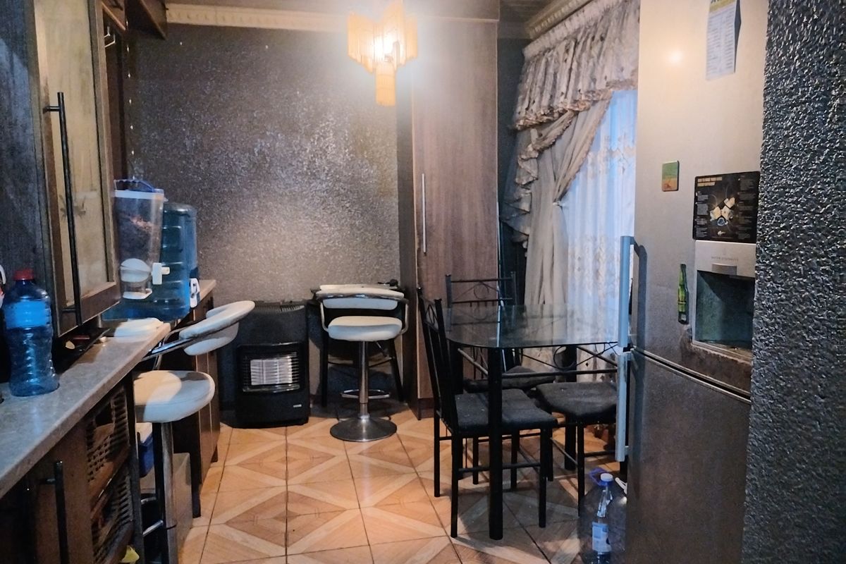 A compact kitchen area featuring built-in cabinetry, tiled flooring, and decorative ceiling cornicing, currently utilized as a combined kitchen and dining space.