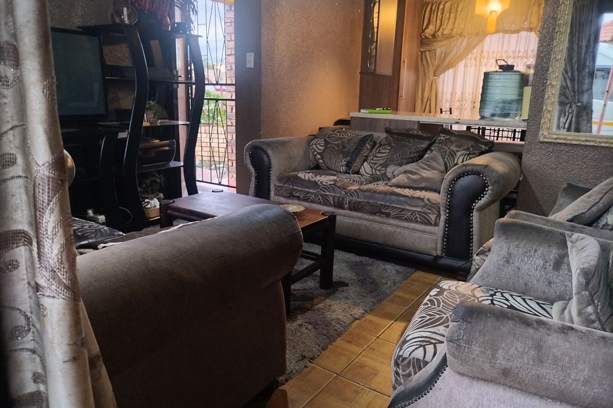 A living room area featuring tiled flooring and a breakfast bar, with a security gate leading to the exterior.
