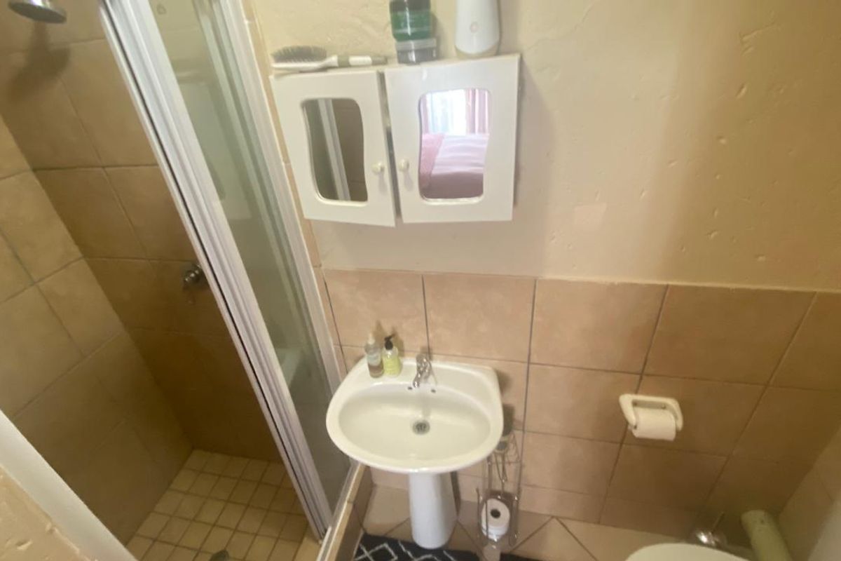 A compact bathroom featuring a shower enclosure with tiled walls, a pedestal basin, and a wall-mounted medicine cabinet.