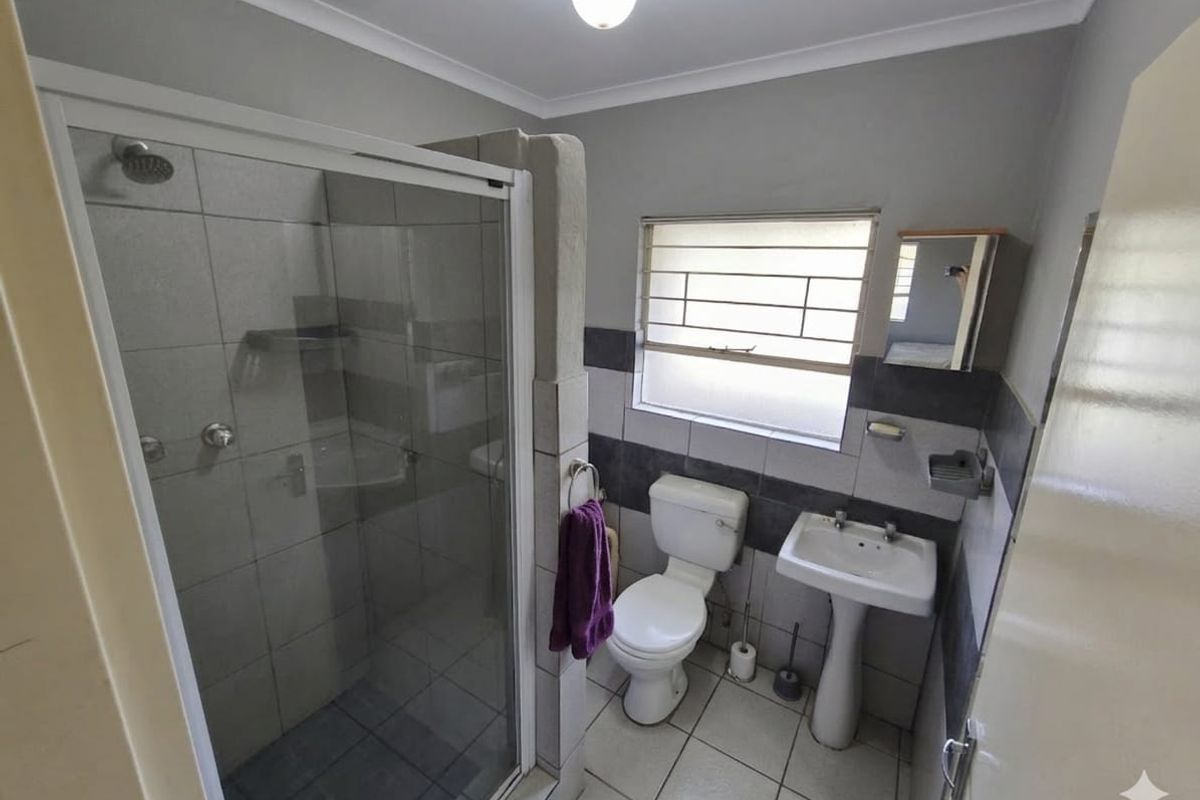 A functional bathroom featuring a glass-enclosed shower, pedestal basin, and toilet with neutral wall and floor tiling.