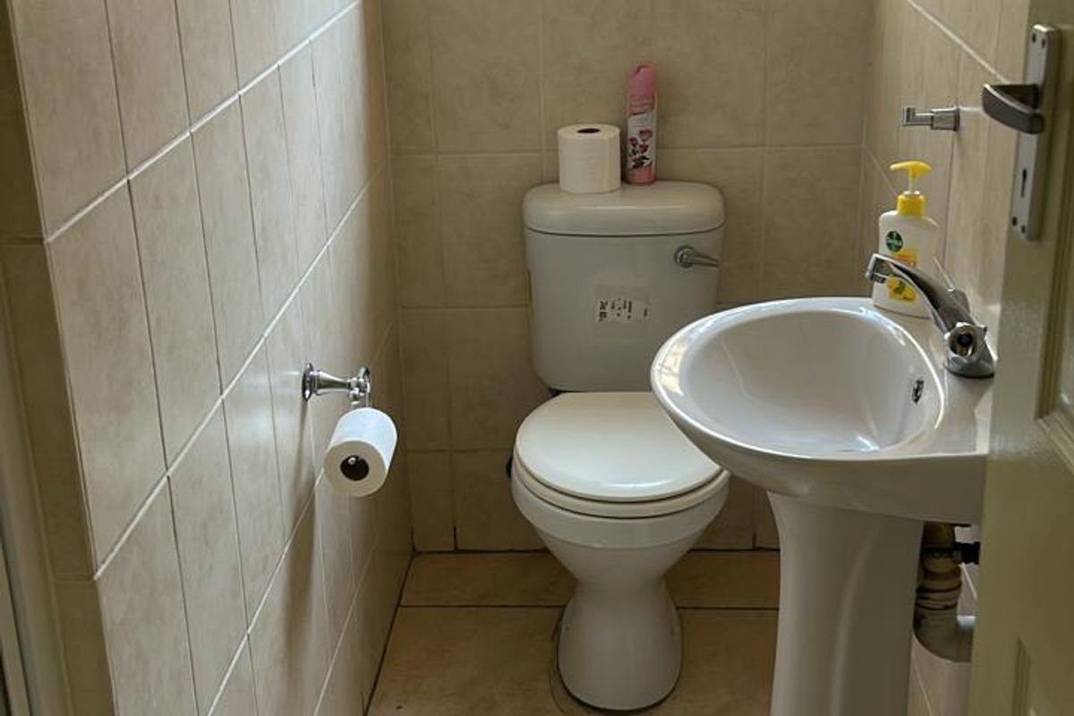 A compact guest bathroom featuring a pedestal basin, a standard toilet, and neutral wall and floor tiling.