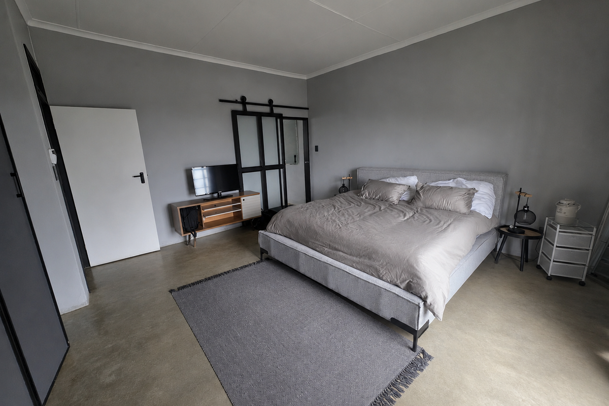 Spacious bedroom featuring polished concrete flooring, neutral grey walls, and a sliding barn-style door leading to an adjacent space.
