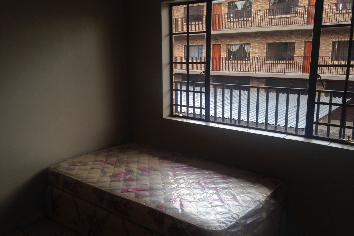 A bedroom featuring tiled flooring and a large window with security bars, offering a view of the adjacent building complex.