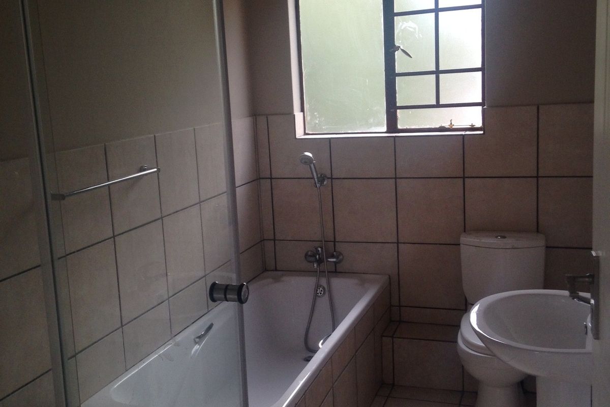 A functional bathroom featuring a tiled bathtub with a shower attachment, a pedestal basin, and a toilet, finished with neutral wall and floor tiles.