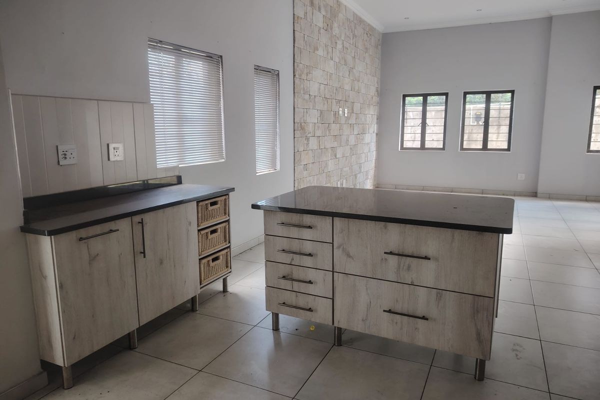 A spacious kitchen area featuring a central island, light wood-finish cabinetry, and a decorative stone veneer feature wall with neutral tiled flooring throughout.