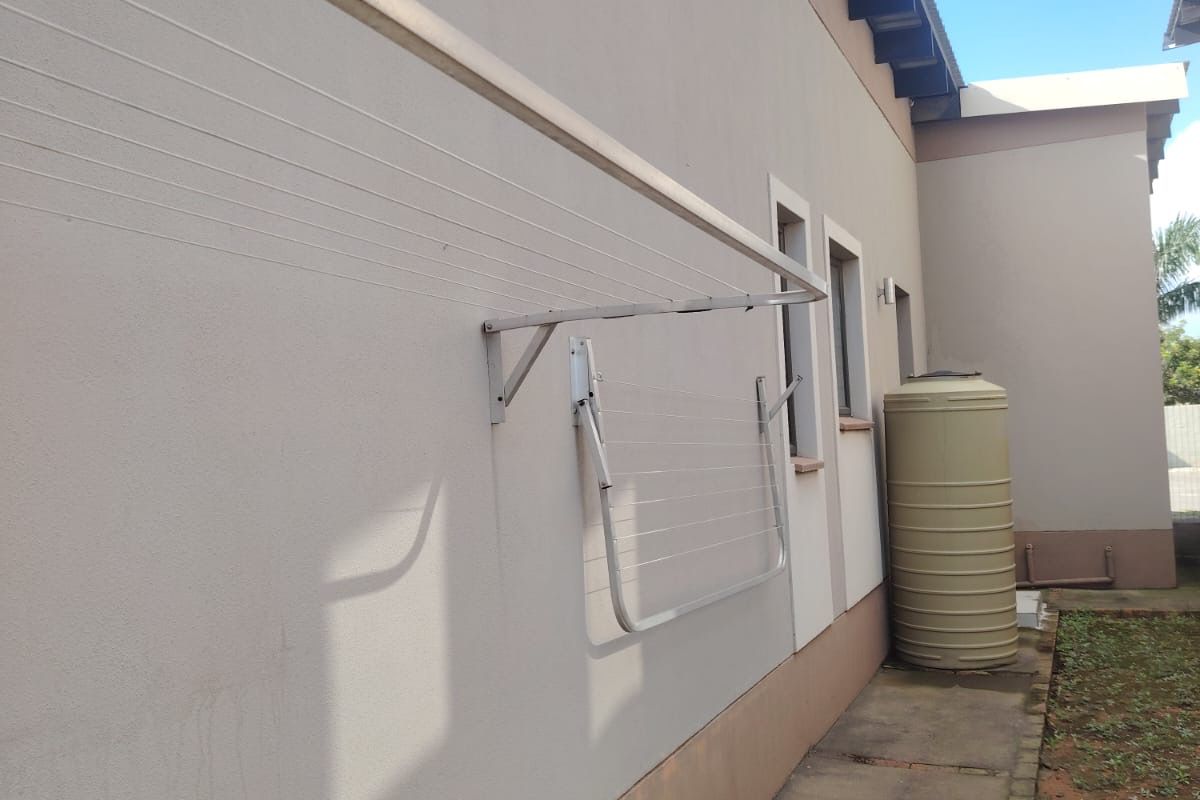 Rear exterior view of the townhouse featuring a paved walkway, wall-mounted clothesline, and a water storage tank.