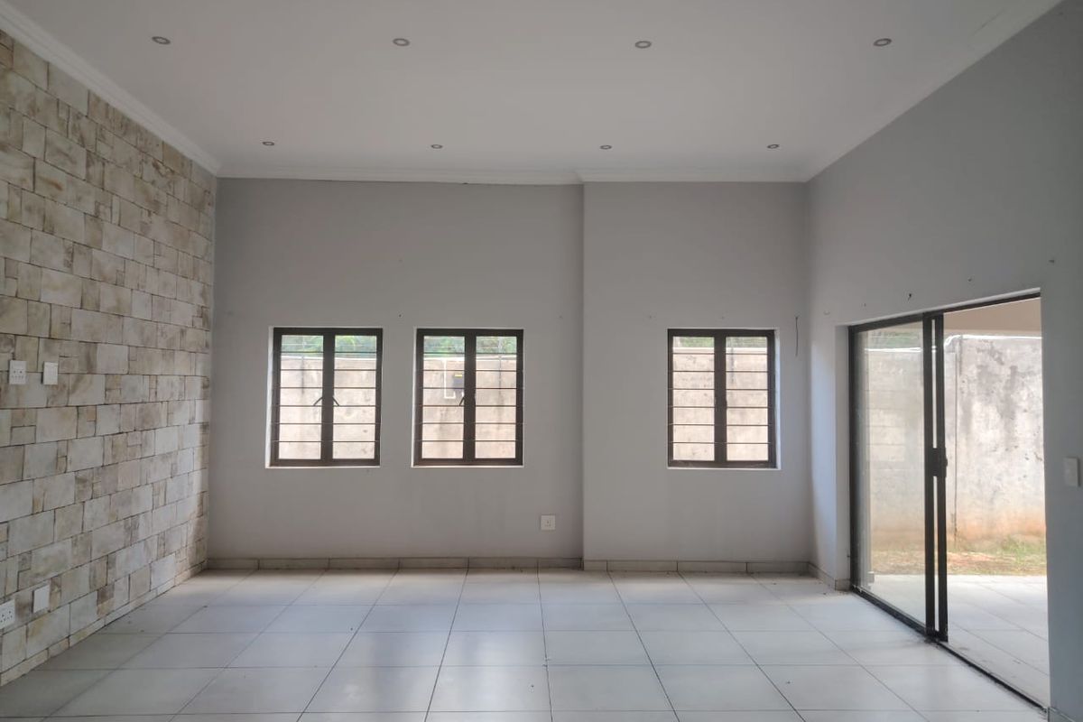 Spacious, empty living area featuring a textured stone accent wall, neutral tiled flooring, recessed lighting, and direct access to the rear patio via sliding doors.