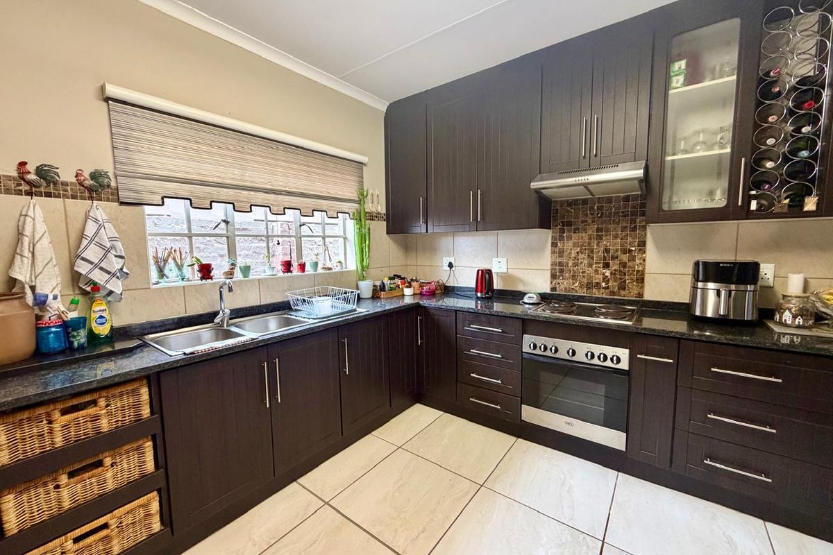A well-maintained kitchen featuring dark wood cabinetry, granite countertops, a built-in oven with hob, extractor fan, and tiled flooring.