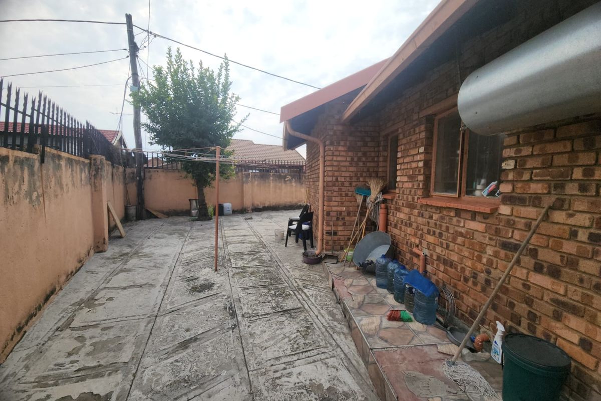 A rear exterior view of the property featuring a paved courtyard, exposed brick facade, and perimeter boundary walls.