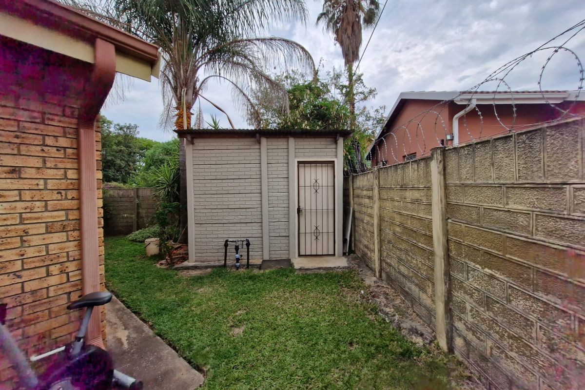 A functional outdoor utility shed located in the rear garden, featuring a secure metal door and adjacent boundary walling.