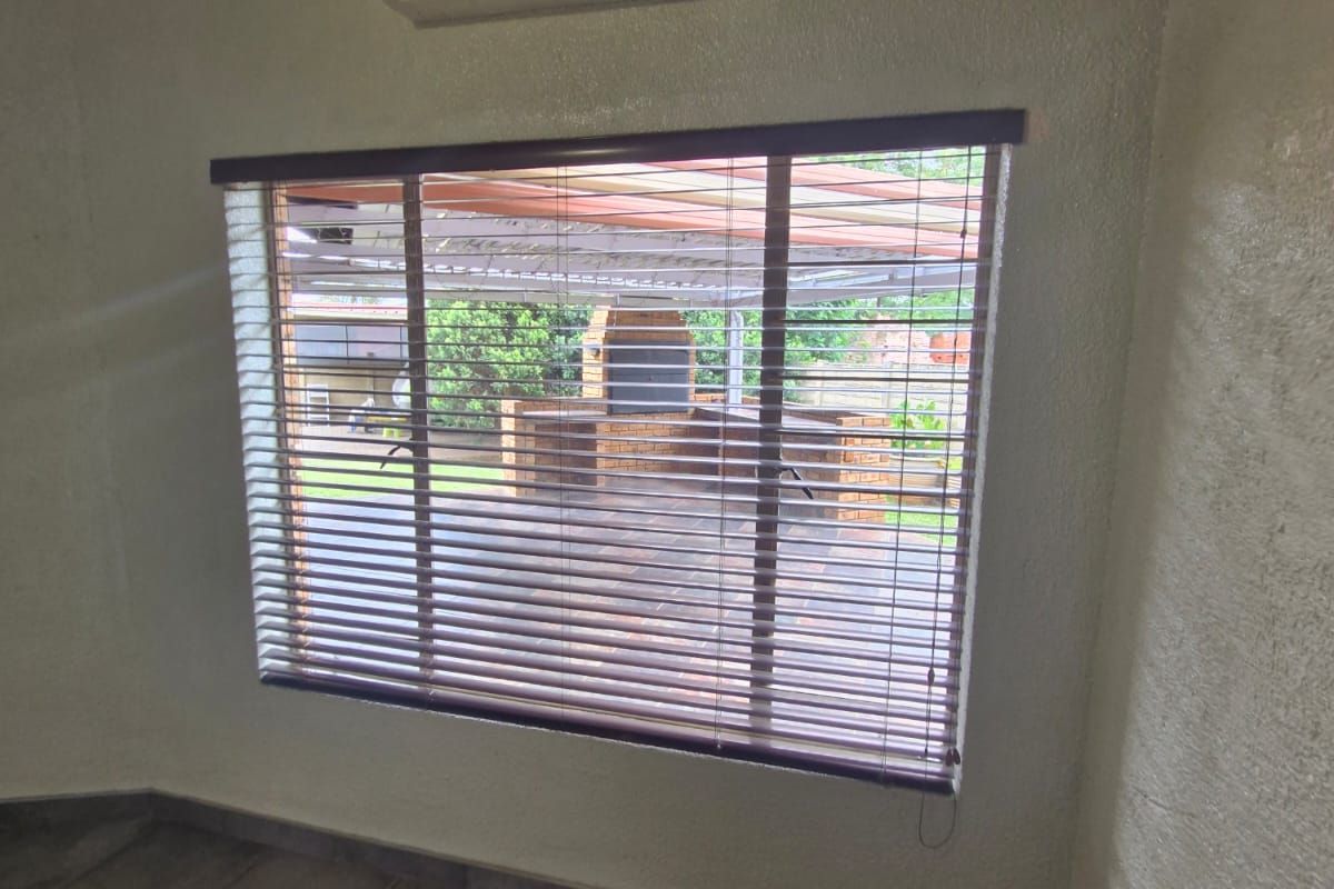 Interior view of a room featuring tiled flooring, a wall-mounted air conditioning unit, and a window overlooking an outdoor patio area.
