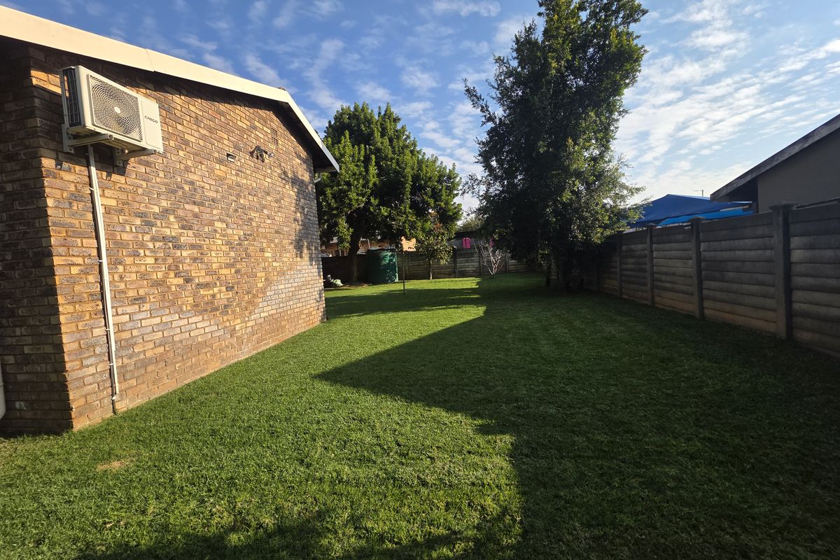 A spacious rear garden featuring a well-maintained lawn, perimeter concrete walling, and an exterior wall-mounted air conditioning unit.