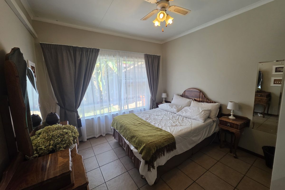 A well-lit bedroom featuring tiled flooring, a ceiling fan, and large windows with curtains, providing a comfortable and functional living space.