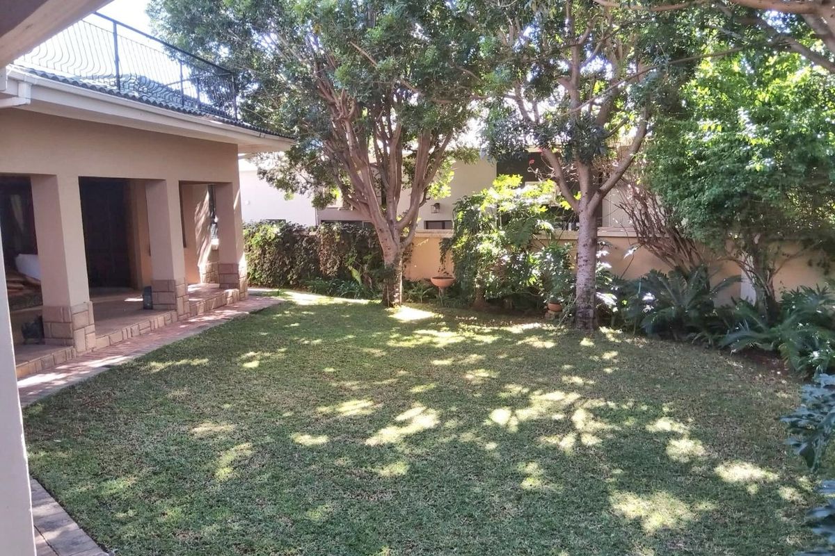 A well-maintained rear garden featuring a lush lawn, mature trees, and a covered patio area attached to the main house structure.