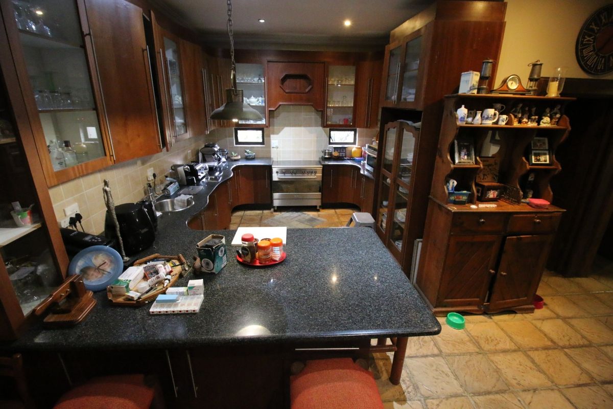 A traditional kitchen featuring dark wood cabinetry, granite countertops, a built-in oven with extractor hood, and tiled flooring.
