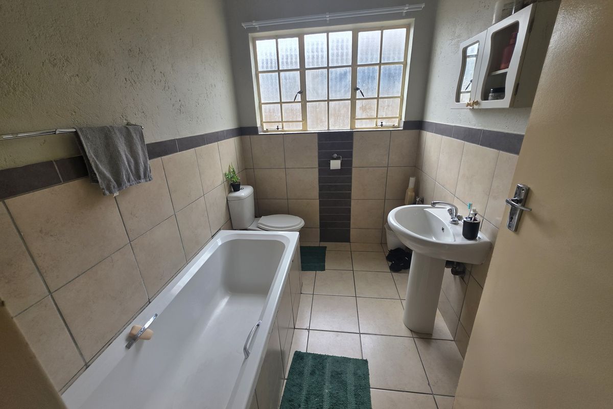 A functional bathroom featuring a standard bathtub, pedestal basin, and toilet with neutral wall and floor tiling.