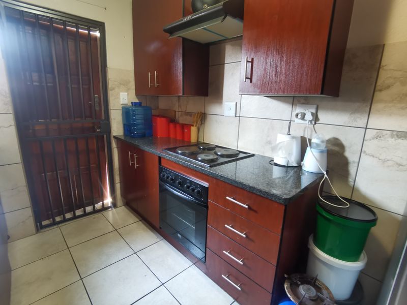Compact kitchen featuring dark wood cabinetry, granite countertops, built-in oven and hob, extractor fan, and tiled splashbacks with direct access to a security gate.