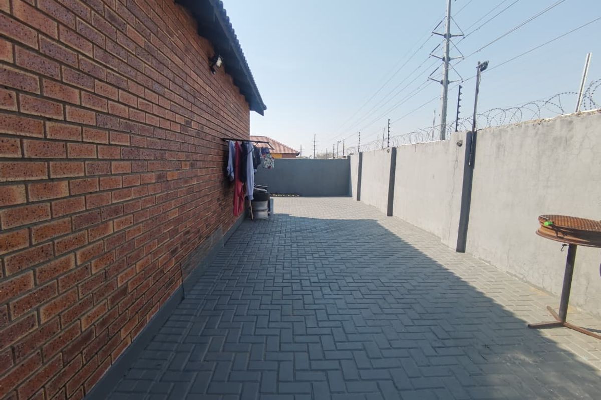 A paved rear exterior area featuring a brick facade, perimeter walling with electric fencing, and an external wall light.
