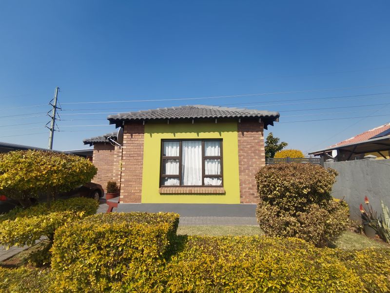 Front elevation of a brick townhouse featuring a tiled roof, aluminium window frames, and a well-maintained garden with a paved driveway.