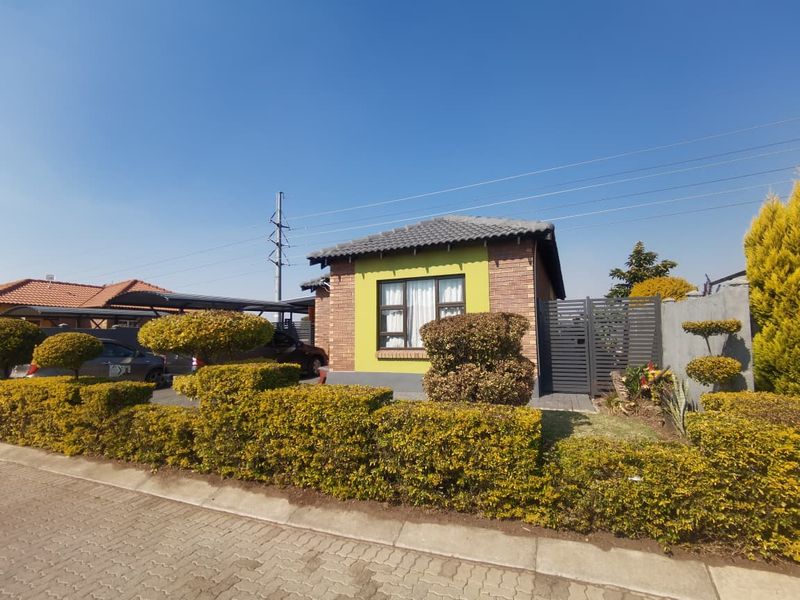 Front view of a townhouse featuring a brick facade, tiled roof, paved driveway, and a secure metal gate entrance.
