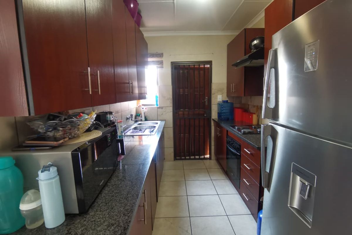 A functional galley-style kitchen featuring dark wood cabinetry, granite countertops, built-in oven, extractor fan, and a secure rear exit door.