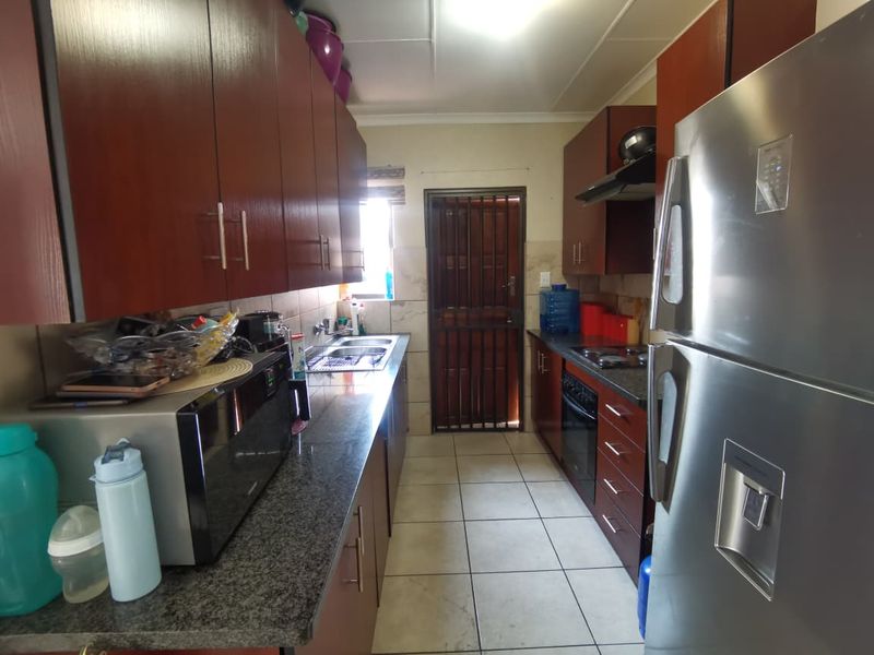 A functional galley-style kitchen featuring dark wood cabinetry, granite countertops, built-in oven, extractor fan, and a secure rear exit door.